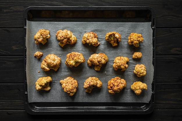 Raw cauliflower seasoned with salt pepper hot paprika and garlic on parchment paper on the baking tray ready to be baked