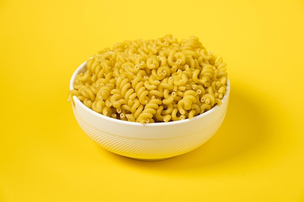 Raw cavatappi cellentani pasta in a plate isolated on yellow background top view