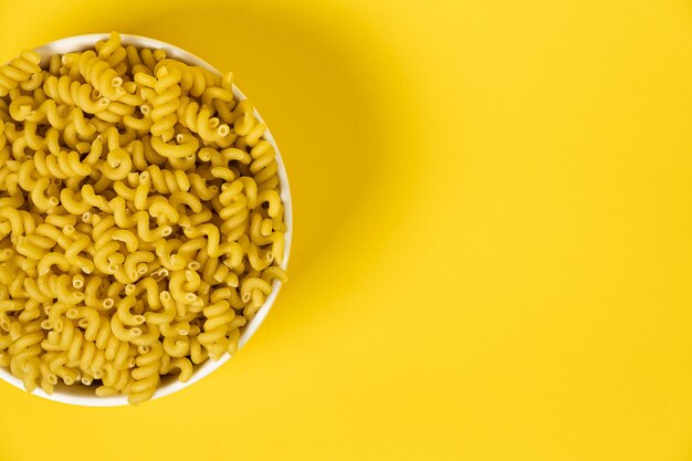 Raw Cavatappi Cellentani pasta in a plate isolated on yellow background top view