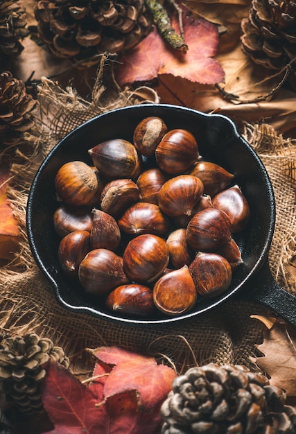 写真 紅葉と松ぼっくりのあるテーブルの上の小さな鉄鍋に生栗