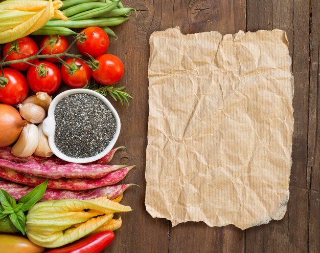 Raw chia seeds in a bowl and fresh vegetables top view on a wooden table