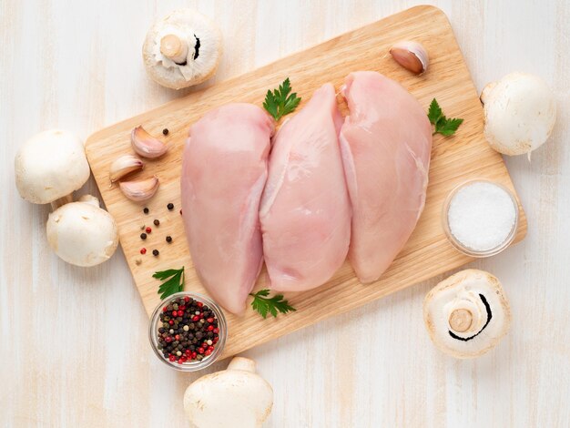 raw chicken breast fillet with spices on wooden board on white wooden table