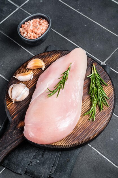 Raw chicken breast fillet on a wooden board with rosemary and garlic poultry meat Black background Top view