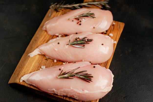 Raw chicken breast fillets, ready for cooking on a wooden cutting board with spices.