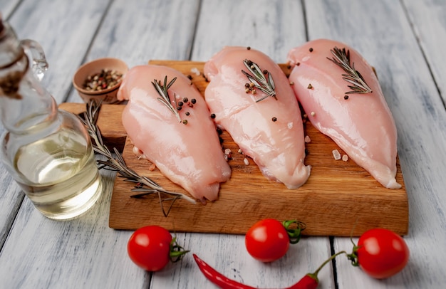 Raw chicken breast fillets, ready for cooking on a wooden cutting board with spices.