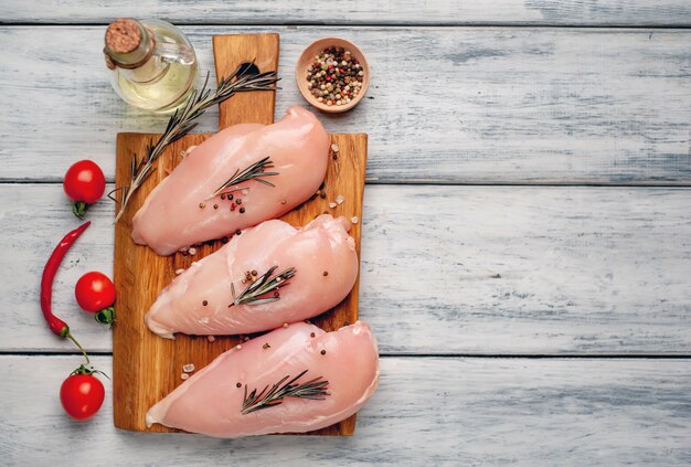 Raw chicken breast fillets, ready for cooking on a wooden cutting board with spices.