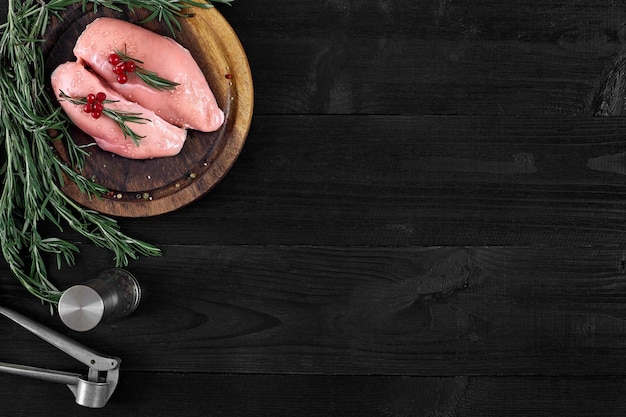 raw chicken breast fillets on wooden cutting board with herbs and spices on a black wooden background. top view with copy space. still life. flat lay.