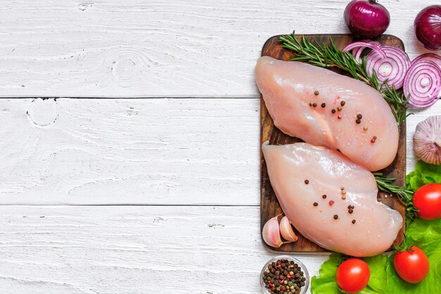 Raw chicken breast fillets on wooden cutting board with vegetables and spices