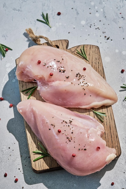 Raw chicken breasts and spices on wooden cutting board