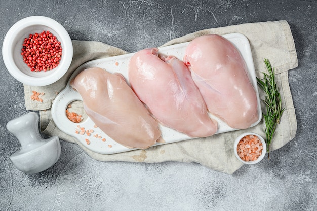 Raw chicken Breasts on a white chopping Board. Organic farm bird. Fresh fillet. Gray background