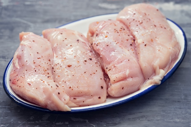 Raw chicken breasts on white dish on ceramic surface