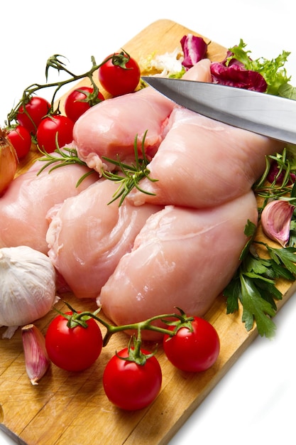 Raw chicken breasts with vegetables on cutting board