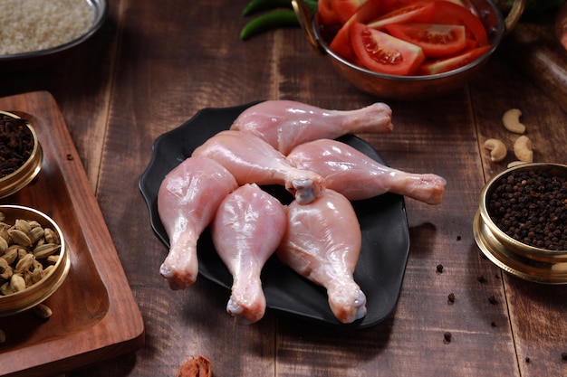 Raw chicken drum sticks arranged on black table ware with cooking ingrediants placed  nearby