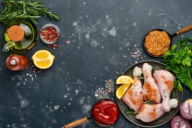 Raw chicken drumsticks with ingredients for cooking on a black stone surface. Top view.