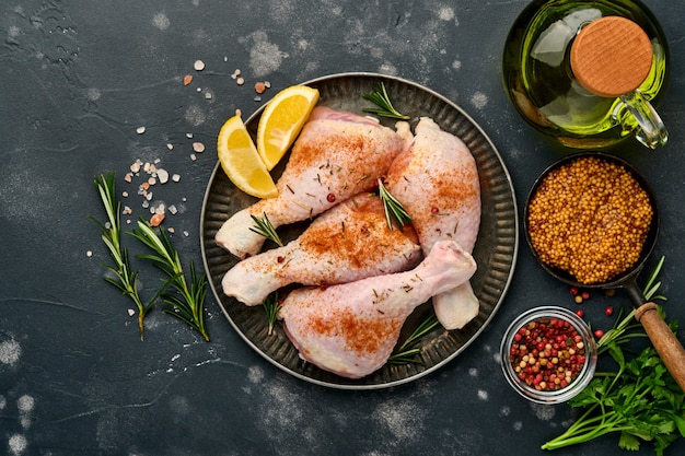 Raw chicken drumsticks with ingredients for cooking on a black stone surface. Top view.