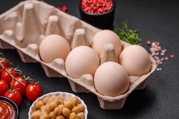 Raw chicken eggs in a box cherry tomatoes chickpeas spices salt and herbs