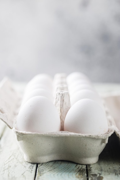 Raw chicken eggs in egg box on white wooden table