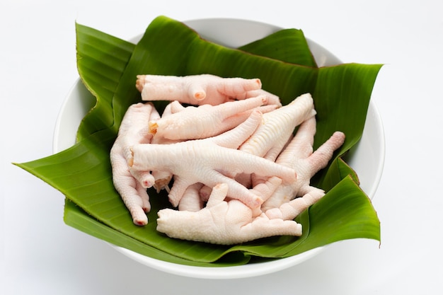 Piedini di pollo crudi in ciotola bianca con foglie di banana