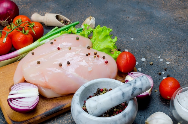 Photo raw chicken fillet on cutting board with spices and herbs.