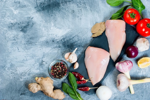 Raw chicken fillet on cutting board with spices and herbs.