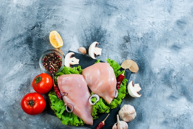 Raw chicken fillet on cutting board with spices and herbs.