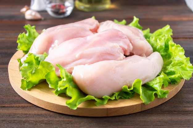 Raw chicken fillet and green salad on a round cutting board on a wooden table background.