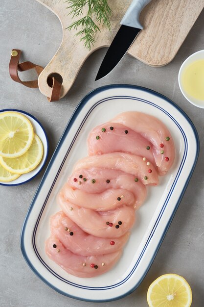 Raw chicken fillet. Meat with breadcrumbs, herbs , lemon and cooking oil. Top view on light stone