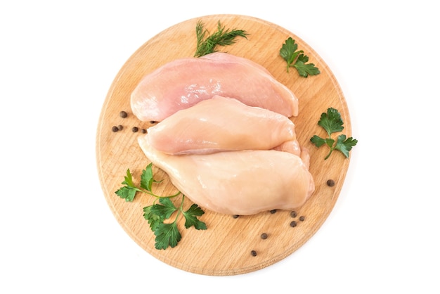 Raw chicken fillet on a round wooden board isolated on white. View from above.