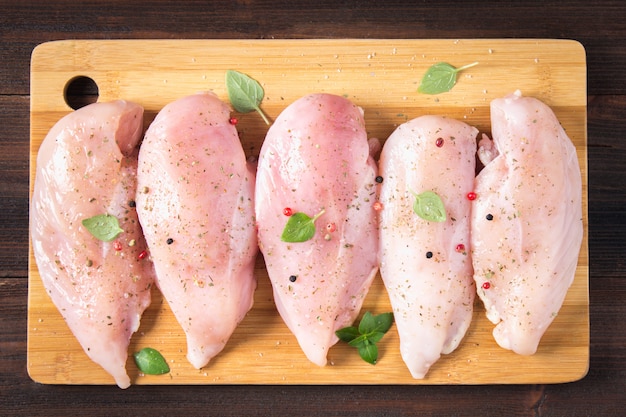 Filetti di pollo crudo su un tagliere sullo sfondo di un tavolo di legno.