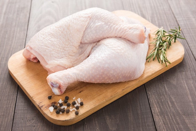 Raw chicken leg on cutting board on wood table