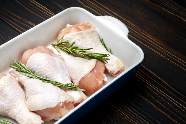 Raw chicken legs in baking dish on a wooden table