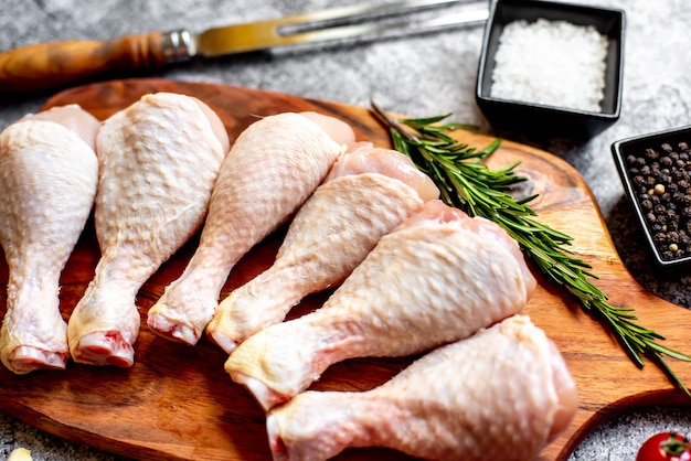 Photo raw chicken legs on a cutting board with salt and pepper on the side.