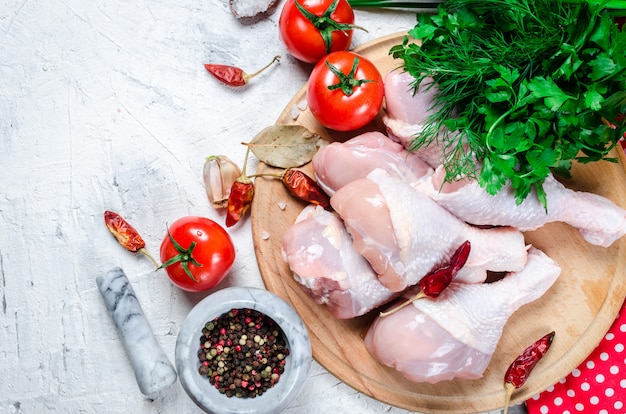 Raw chicken legs on cutting board with spices and herbs.