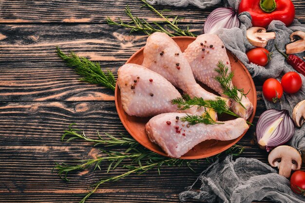 Raw chicken legs with fresh vegetables and rosemary and spices on a black wooden background Top view Free space for text