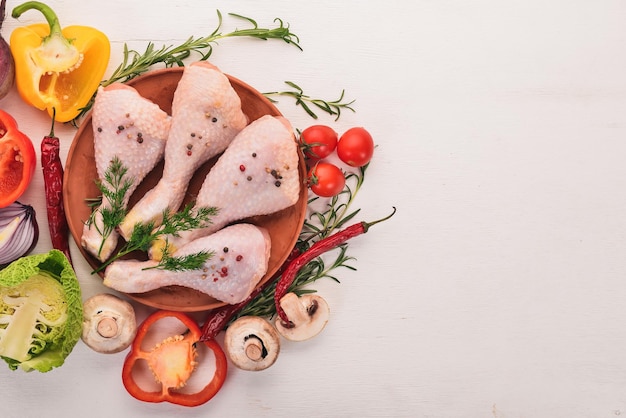 Raw chicken legs with fresh vegetables and rosemary and spices on a white wooden background. Top view. Free space for text.