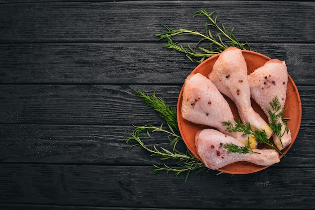 Raw chicken legs with rosemary and spices on a black wooden background Top view Free space for text