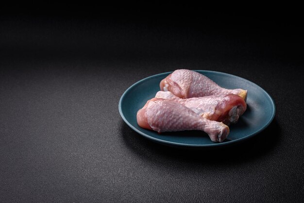 Photo raw chicken legs with salt spices and herbs on a dark concrete background