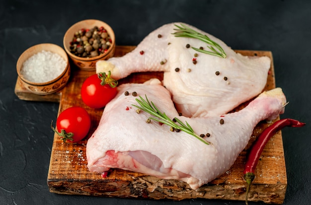 Raw chicken legs with spices and herbs ready for cooking on a stone background.