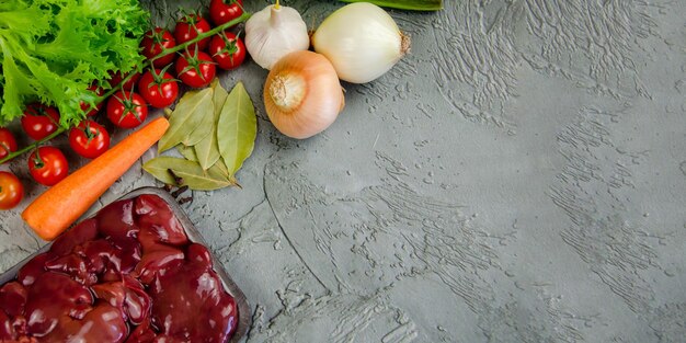 Raw chicken liver vegetables and spices for making pate on a textured concretegray background