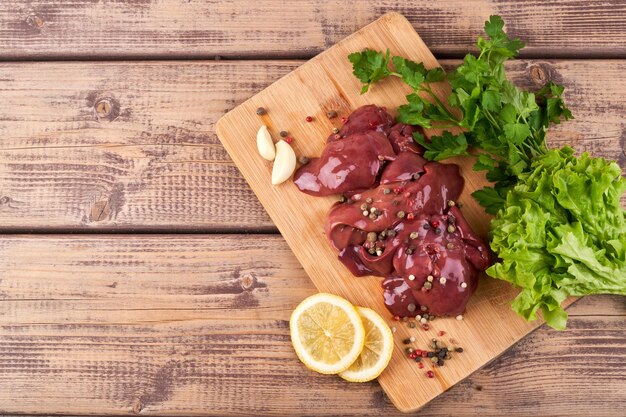 Photo raw chicken liver on a wooden board, beautifully served with pepper, lemon and herbs