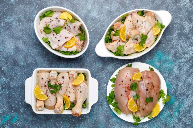 Raw chicken meat fillet, thigh, wings and legs in ceramic oven plates with herbs ,spices,lemon and garlic on grey. Top view