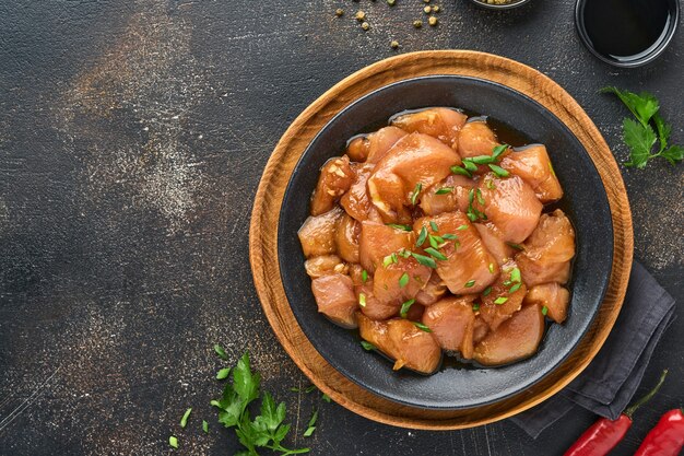 Сырое куриное мясо, маринованное в соевом соусе терияки, луком и перцем в черной тарелке на темном сланцевом, каменном или бетонном фоне. Вид сверху с копией пространства.