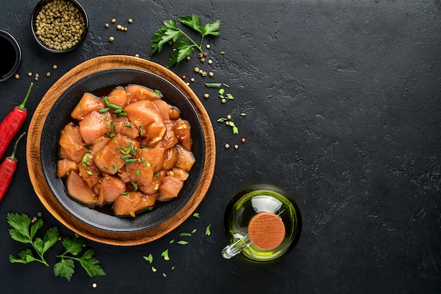 Raw chicken meat marinated in teriyaki soy sauce, onions and pepper in a black plate on a dark slate, stone or concrete background. Top view with copy space.