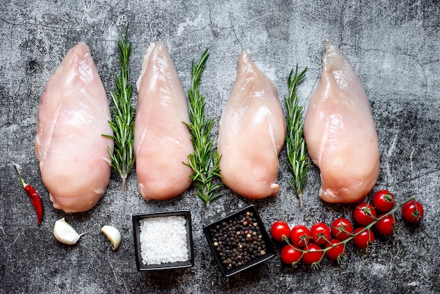 Foto carne di pollo cruda su un tavolo con rosmarino e pomodori