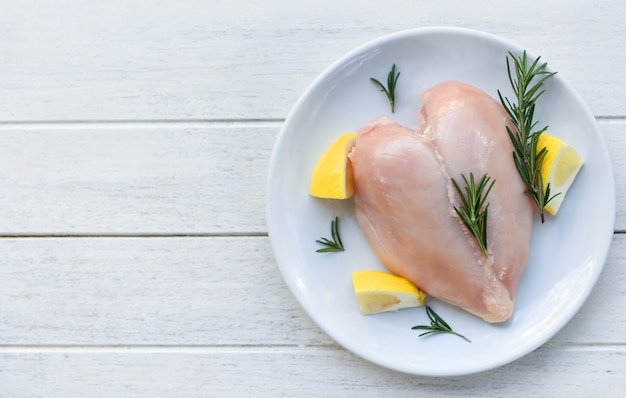 Raw chicken meat with rosemary and lemon - fresh raw chicken breast heart shaped fillet on white plate , top view