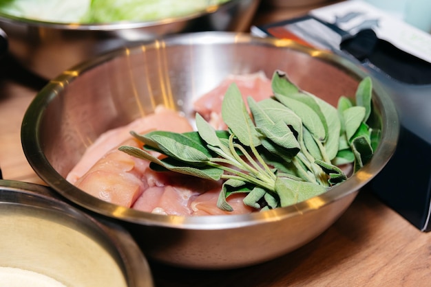 Raw chicken meat with sage in a stainless steel bowl on the table