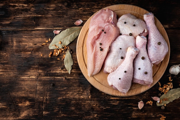 Carne di pollo cruda con spezie su tavola di legno su fondo di legno scuro.