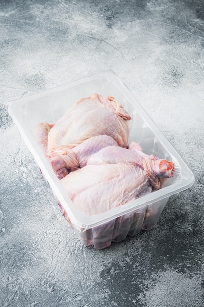 灰色のテーブルに、プラスチックで密封されたプラスチックの箱に入った生の鶏肉