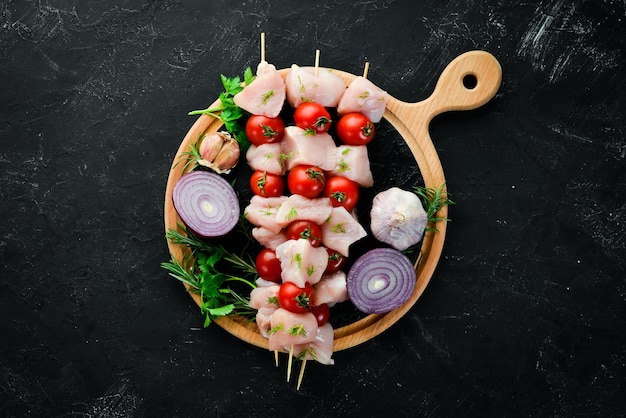 Raw chicken shish kebab with cherry tomatoes Barbecue On a black stone background Top view Free copy space