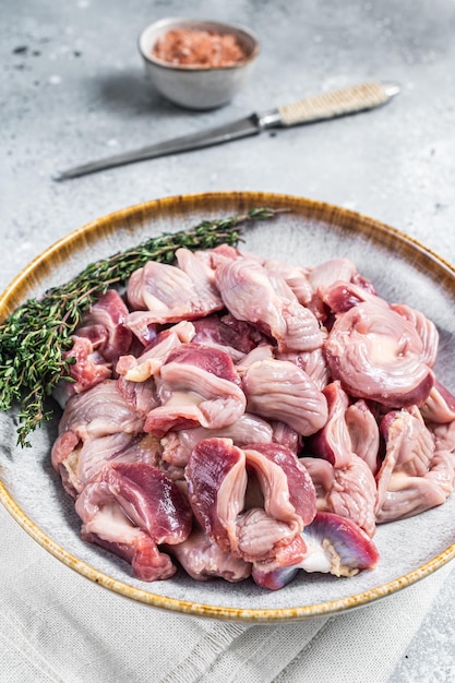Raw chicken stomachs offals in a plate with herbs Gray background Top view